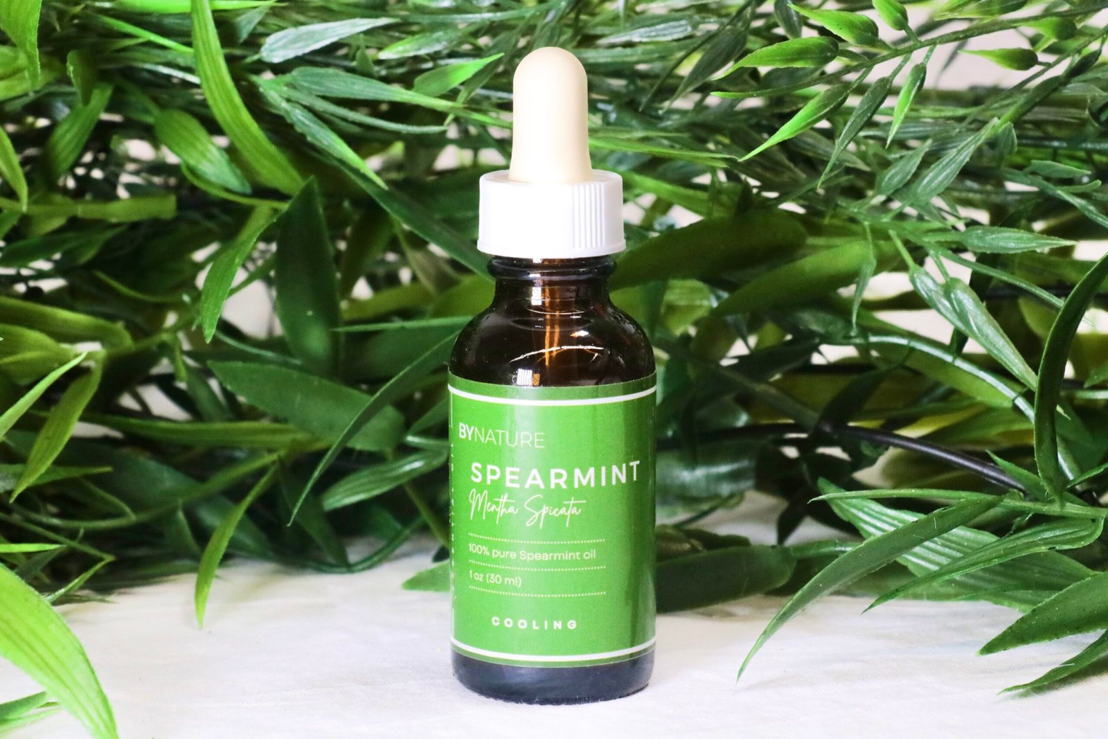 A bottle of pure spearmint essential oil with fresh leaves in the background.