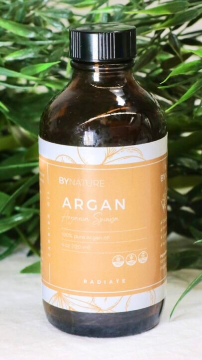 A bottle of pure argan carrier oil with fresh leaves in the background.