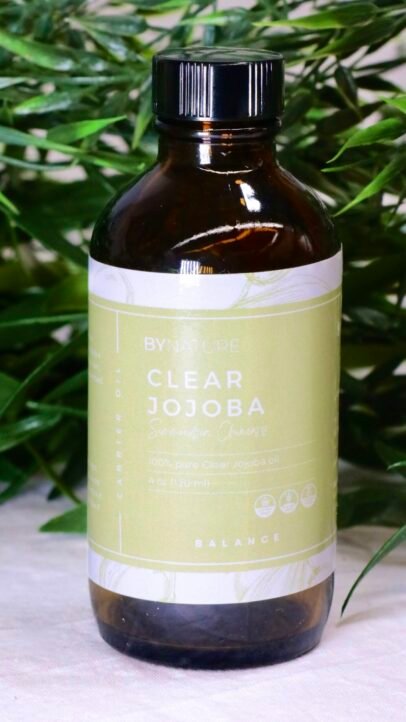 A bottle of pure clear jojoba carrier oil with fresh leaves in the background.
