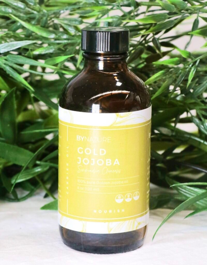 A bottle of pure gold jojoba carrier oil with fresh leaves in the background.