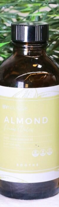 A bottle of pure almond carrier oil with fresh leaves in the background.