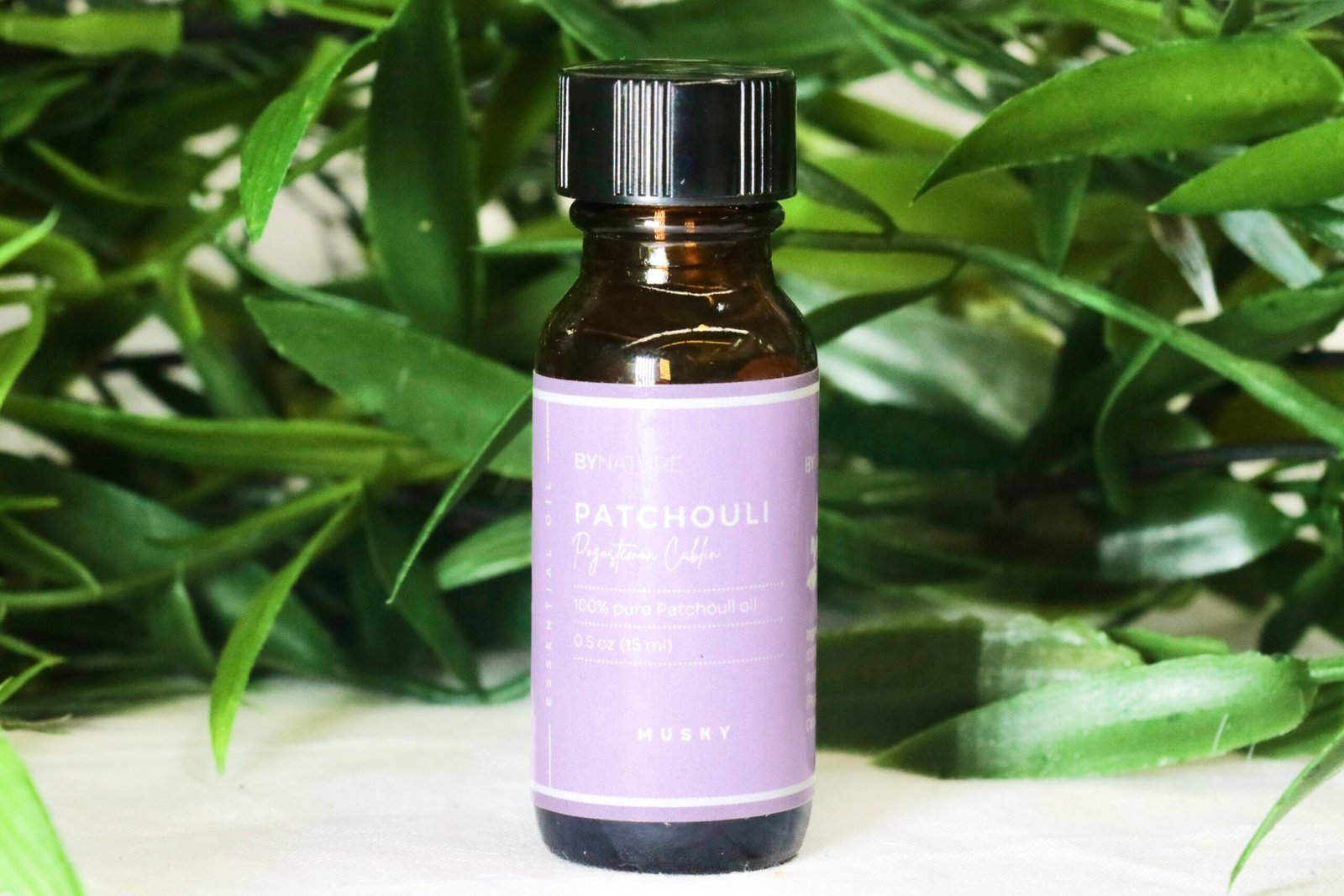 A bottle of pure patchouli essential oil with fresh leaves in the background.