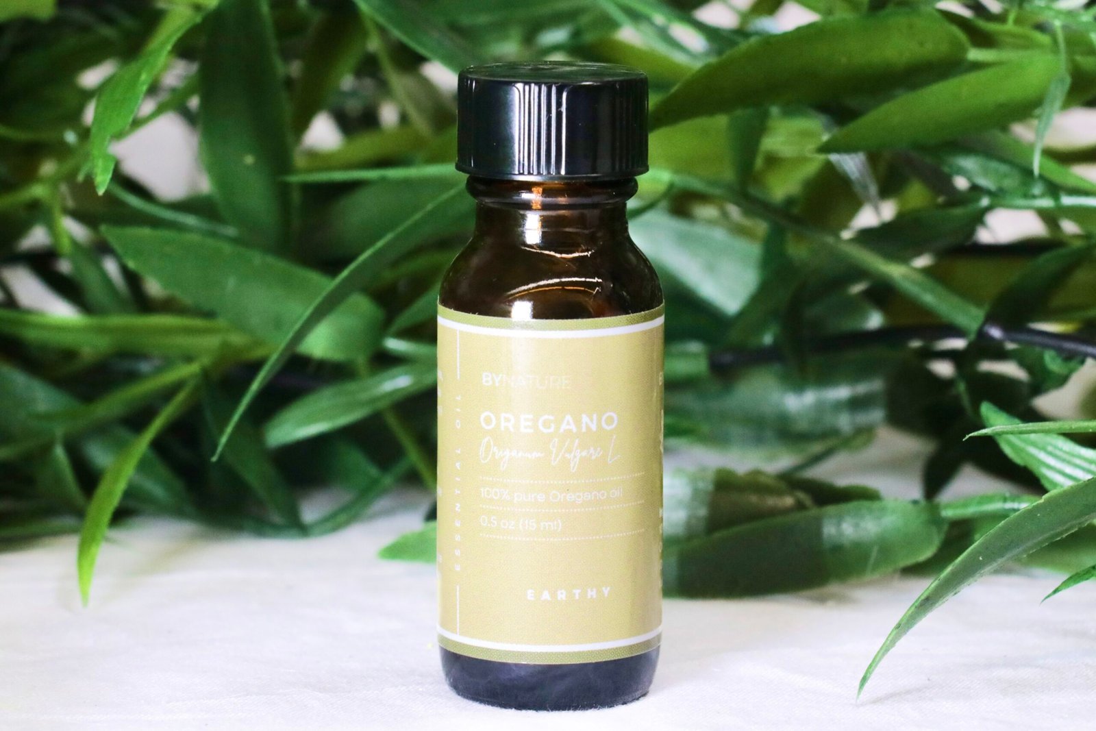A bottle of pure oregano essential oil with fresh leaves in the background.