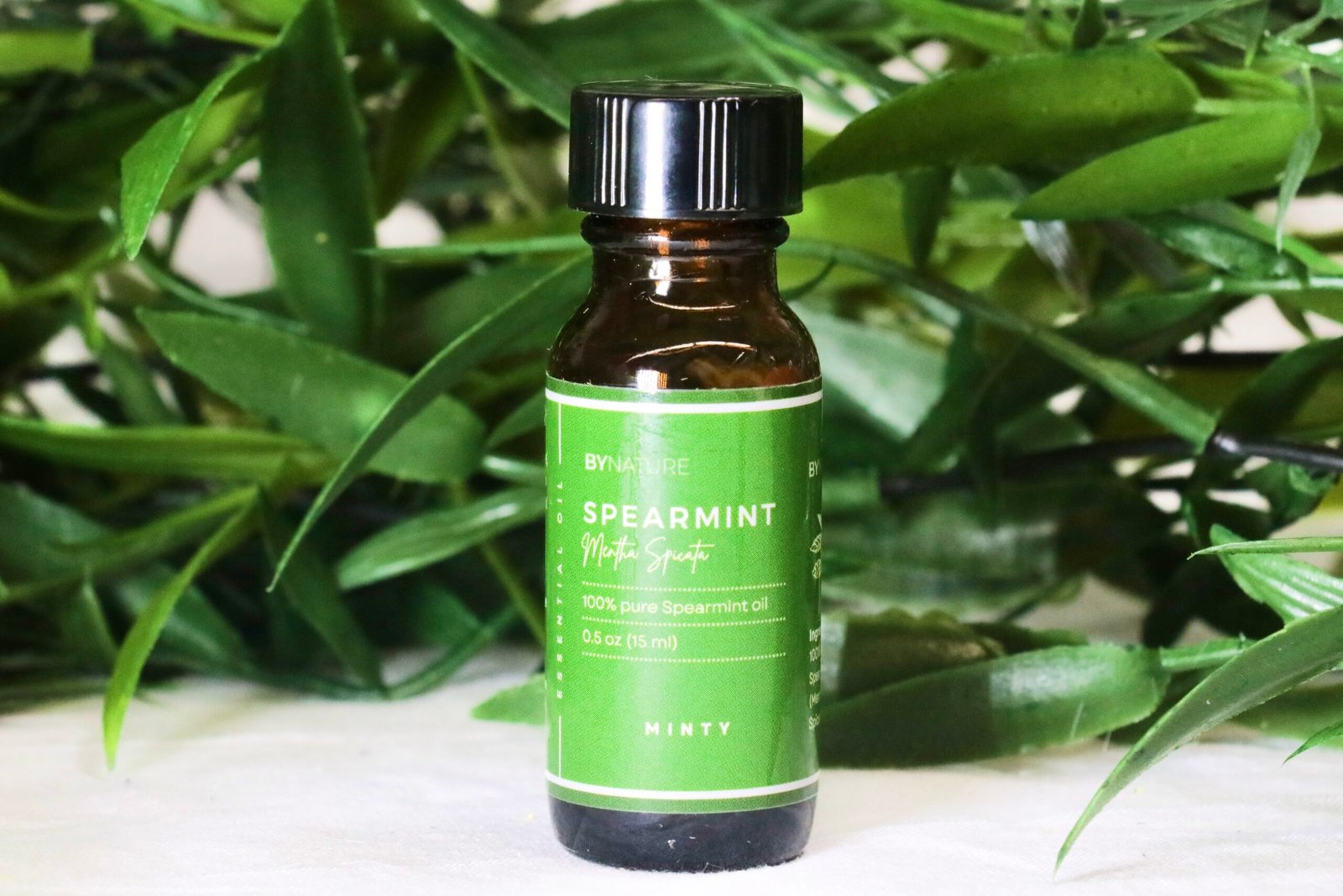 A bottle of pure spearmint essential oil with fresh leaves in the background.