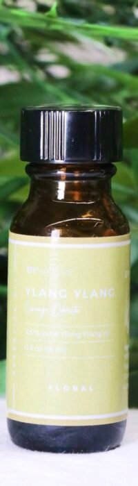 A bottle of pure ylang ylang essential oil with fresh leaves in the background.