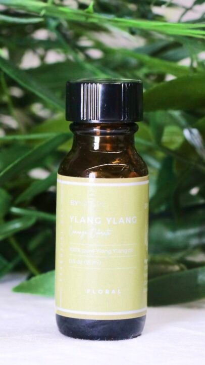 A bottle of pure ylang ylang essential oil with fresh leaves in the background.