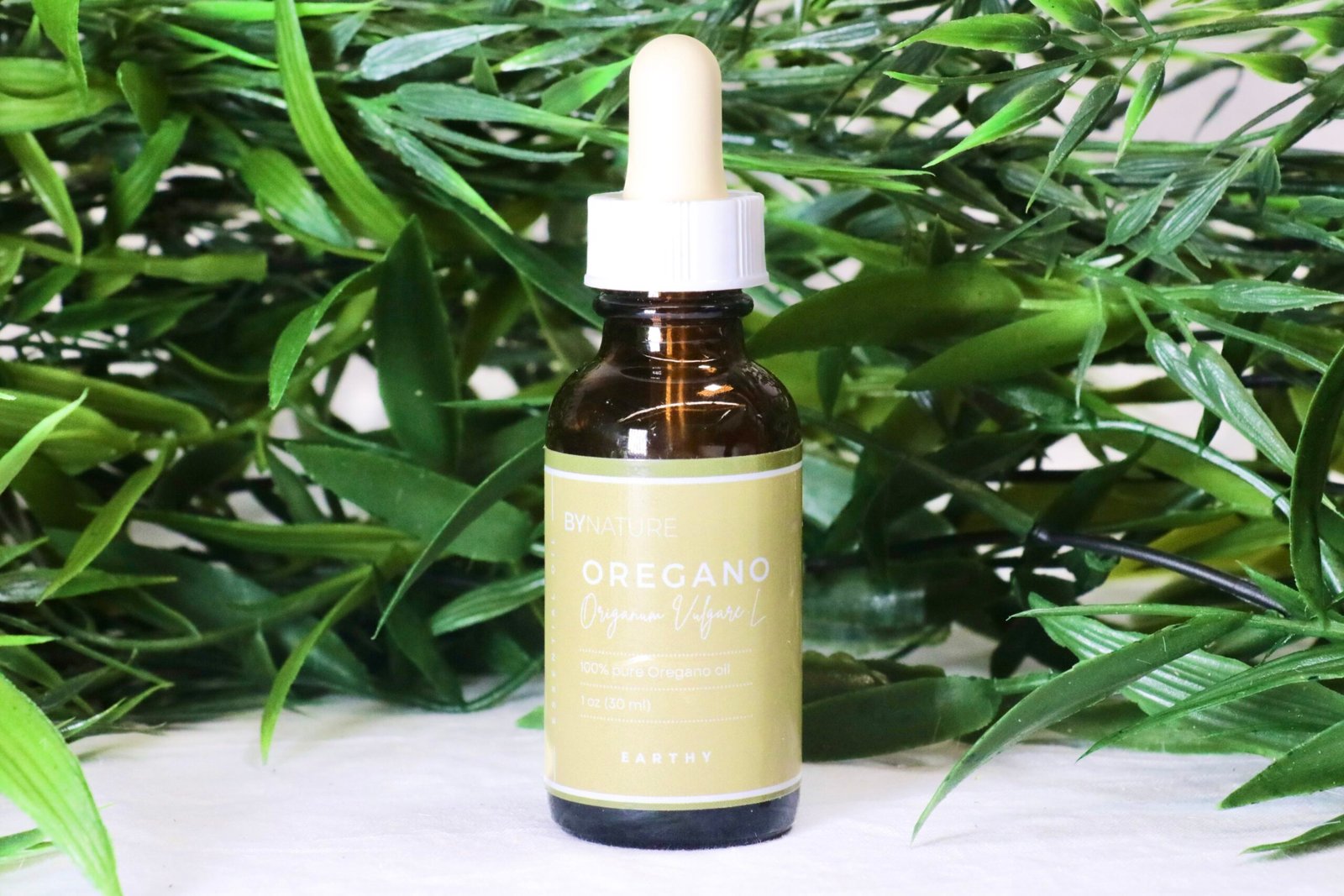 A bottle of pure oregano essential oil with fresh leaves in the background.