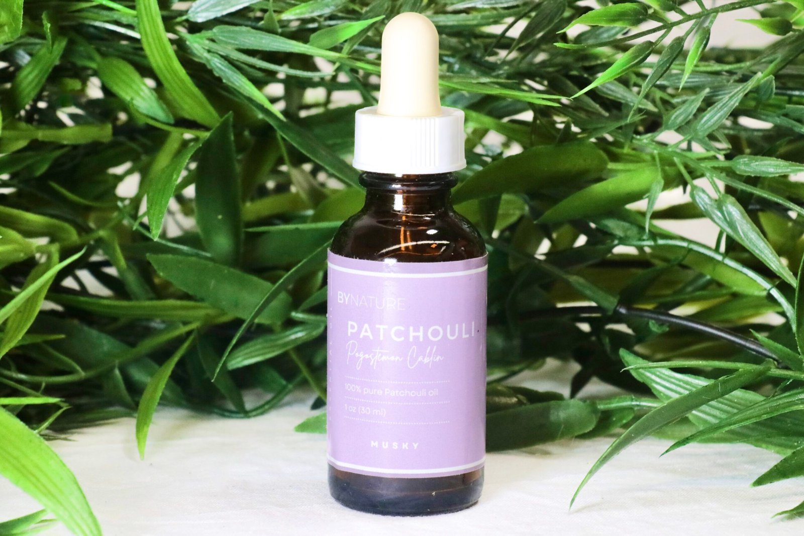 A bottle of pure patchouli essential oil with fresh leaves in the background.