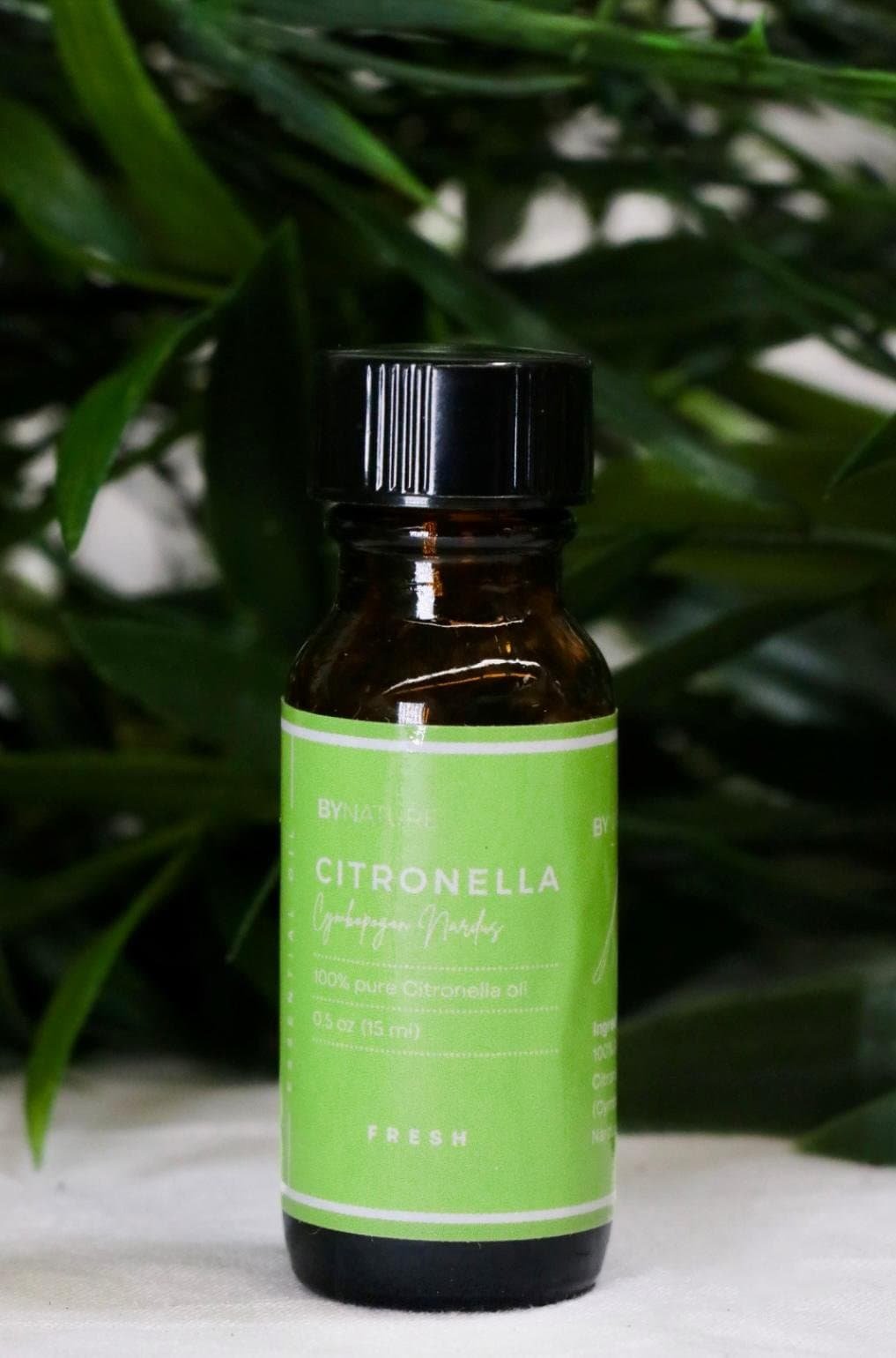 A bottle of pure citronella essential oil with fresh leaves in the background.