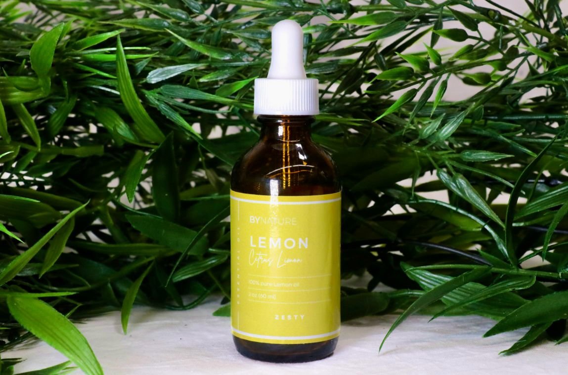 A bottle of pure lemon essential oil with fresh leaves in the background.