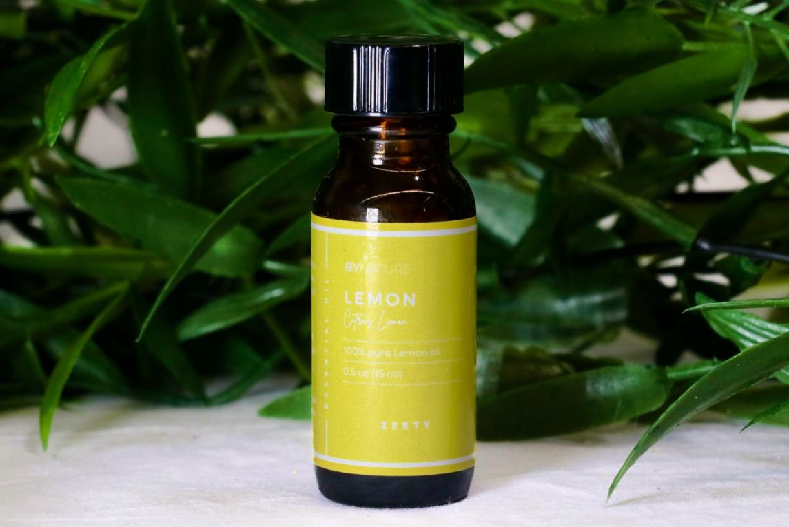 A bottle of pure lemon essential oil with fresh leaves in the background.